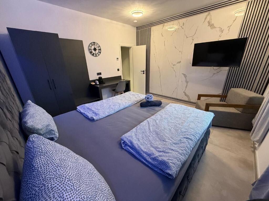 A modern bedroom with two beds, a desk, a chair, and a TV.