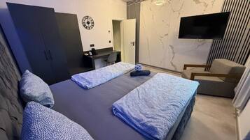 A modern bedroom with two beds, a desk, a chair, and a TV.