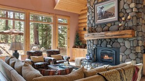 A cozy living room with a stone fireplace, large windows, and comfortable seating. - GH261 | Amazing Luxury home sure to be your new favorite! (Black Butte Ranch)