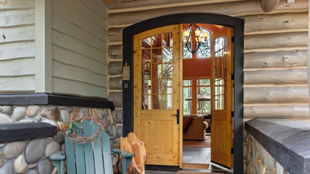 A wooden cabin entrance with a stone wall, a wooden door, and a bench outside. - GH261 | Amazing Luxury home sure to be your new favorite! (Black Butte Ranch)
