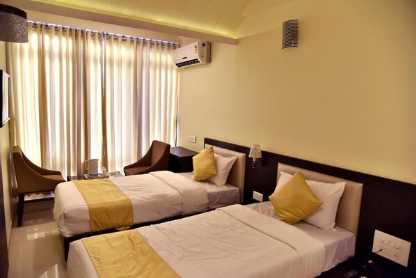 A hotel room with two beds, a desk, a chair, and a window with curtains. - Hotel Time Square (Thane)