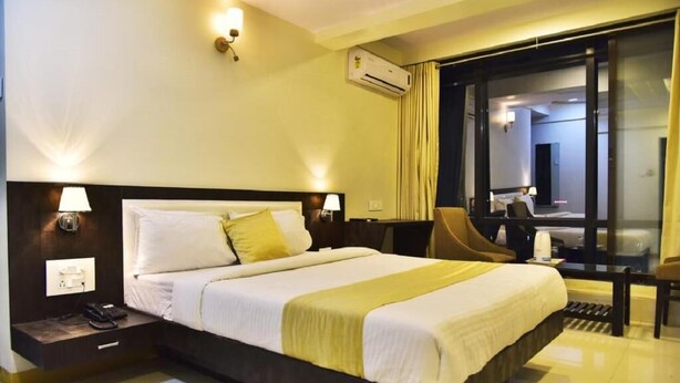 A hotel room with a large bed, bedside lamps, a desk, and a chair. - Hotel Time Square (Thane)