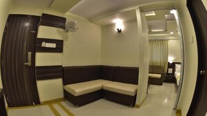 A corner room with a sofa, a fan, and a bed. - Hotel Time Square (Thane)
