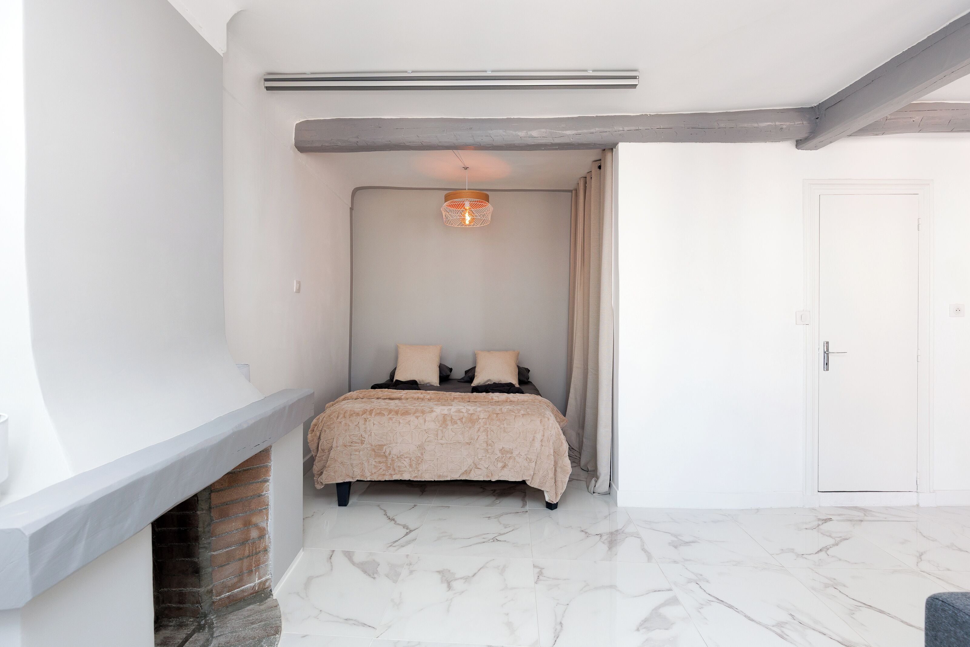 A bedroom with a bed, a fireplace, a ceiling light, and a door.