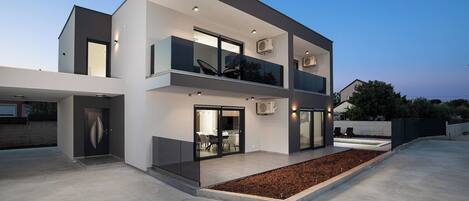 A modern two-story house with a balcony, large windows, and a well-lit entrance.