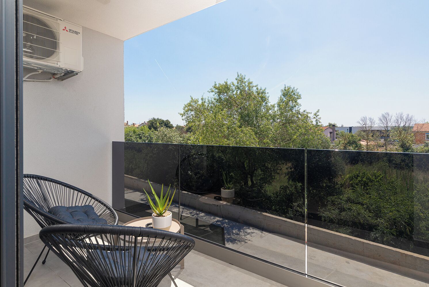 A balcony with two black chairs, a potted plant, and a glass barrier.