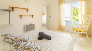 A bedroom with a bed, two pillows, a rolled towel, a chair, and a window with curtains.