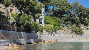 A coastal area with a stone wall, clear water, and buildings with balconies.