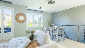 A spacious living room with a large sofa, a dining area with a glass table and chairs, and a balcony with a railing.