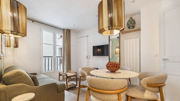Un salon moderne avec un canapé, des fauteuils, une table ronde et un téléviseur fixé au mur.