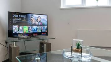 Un téléviseur diffusant la série « Emily à Paris » sur Netflix, avec une table en verre devant et une petite plante posée sur la table.