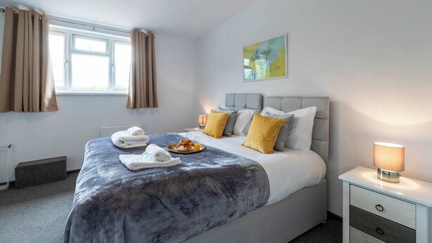 Une chambre d’hôtel avec un grand lit, une table de chevet avec une lampe, une fenêtre avec des rideaux et un tableau au mur.