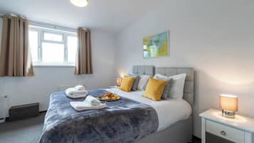 Une chambre d’hôtel avec un grand lit, une table de chevet avec une lampe, une fenêtre avec des rideaux et un tableau au mur.