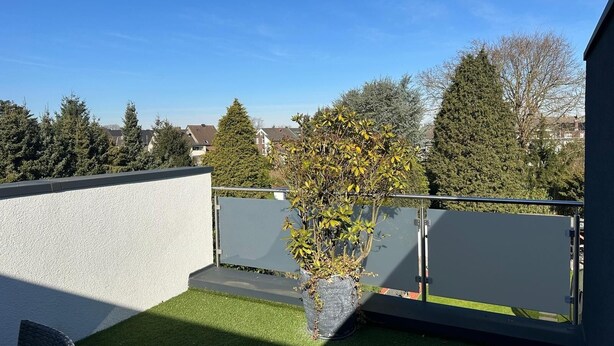 Una terrazza sul tetto con un piccolo albero, una ringhiera e vista su case sullo sfondo.