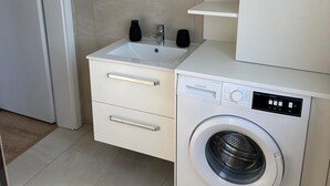 Un bagno moderno con lavandino, specchio, porta asciugamani e una lavatrice a incasso.
