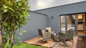 Un patio esterno moderno con mobili in vimini, un pavimento in legno e una porta vetrata che dà su una zona cucina.