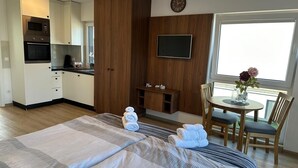 Una camera d'hotel con un letto, una TV, un'area ristorazione con tavolo e sedie, un armadietto in legno e una finestra con vista.