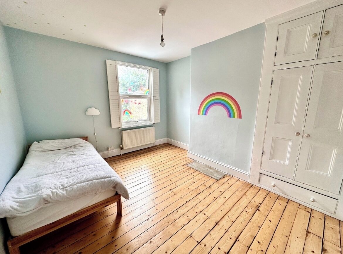 Um quarto com piso de madeira, uma cama, uma janela e um guarda-roupa.
