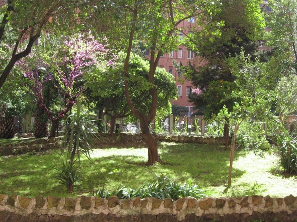 Un jardin agrémenté de divers arbres et arbustes, un mur de pierre et un bâtiment en arrière-plan.