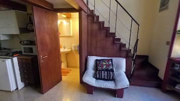 Un ambiente compatto con angolo cottura, zona pranzo e una scala che conduce a un livello superiore.