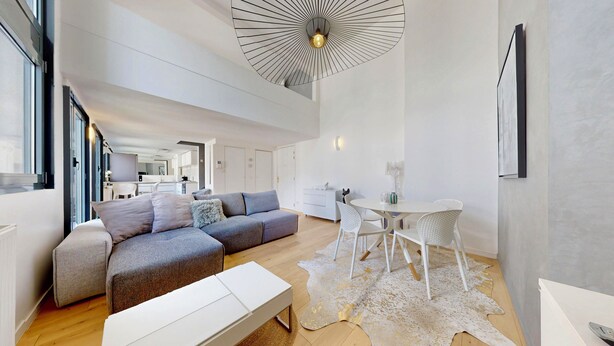 Un salon moderne avec un canapé d’angle, une table basse blanche et un coin repas comprenant une table et des chaises blanches.
