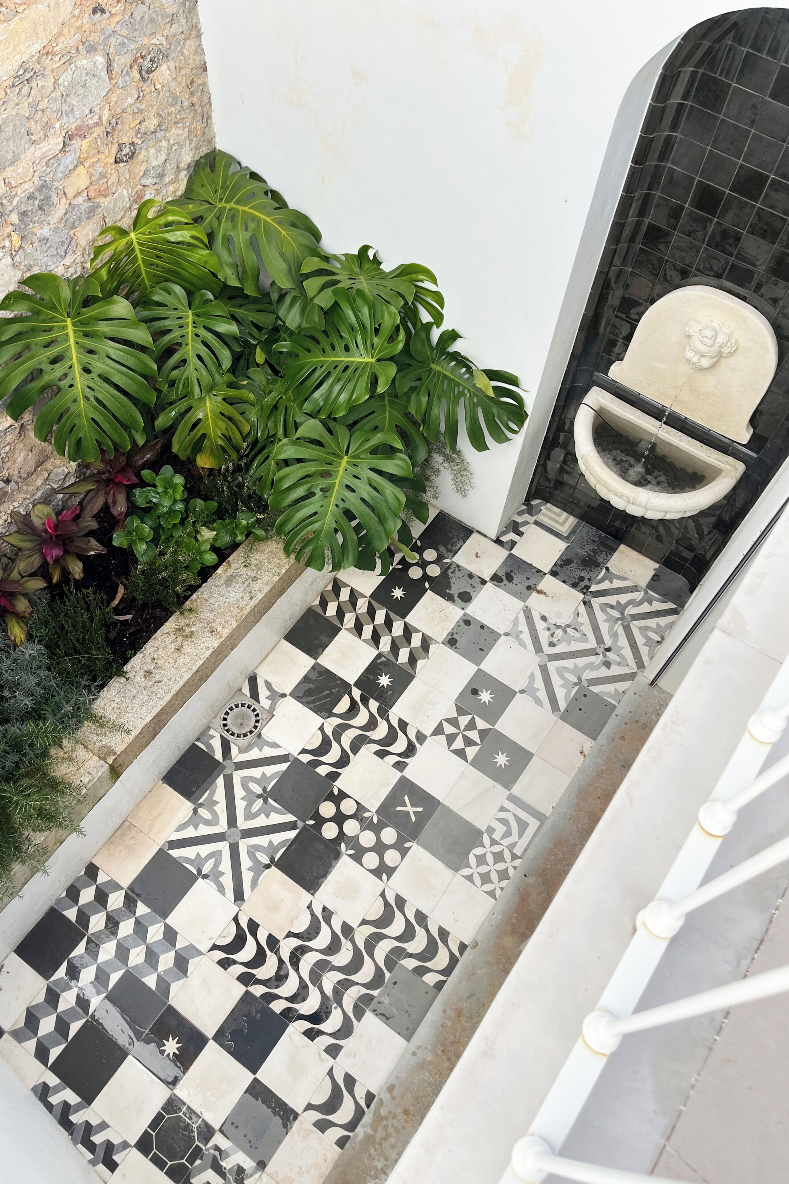 A tiled floor with a geometric pattern, a stone wall, and a planter with green foliage.