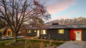 A two-story house with a dark exterior, a front porch, and a well-maintained garden. - Family Retreat - Backyard Games + Movie Room - Sleeps 16 (Orem)