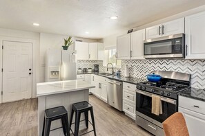 Une cuisine moderne avec des meubles blancs, un réfrigérateur en acier inoxydable, un four à micro-ondes, une cuisinière et un lave-vaisselle.