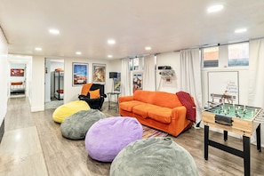 Un salon avec un baby-foot, un canapé orange, des fauteuils en forme de poire et divers posters accrochés aux murs.