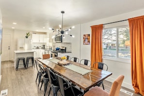 Une cuisine moderne avec des meubles blancs, un îlot central et un coin repas comprenant une table et des chaises en bois.