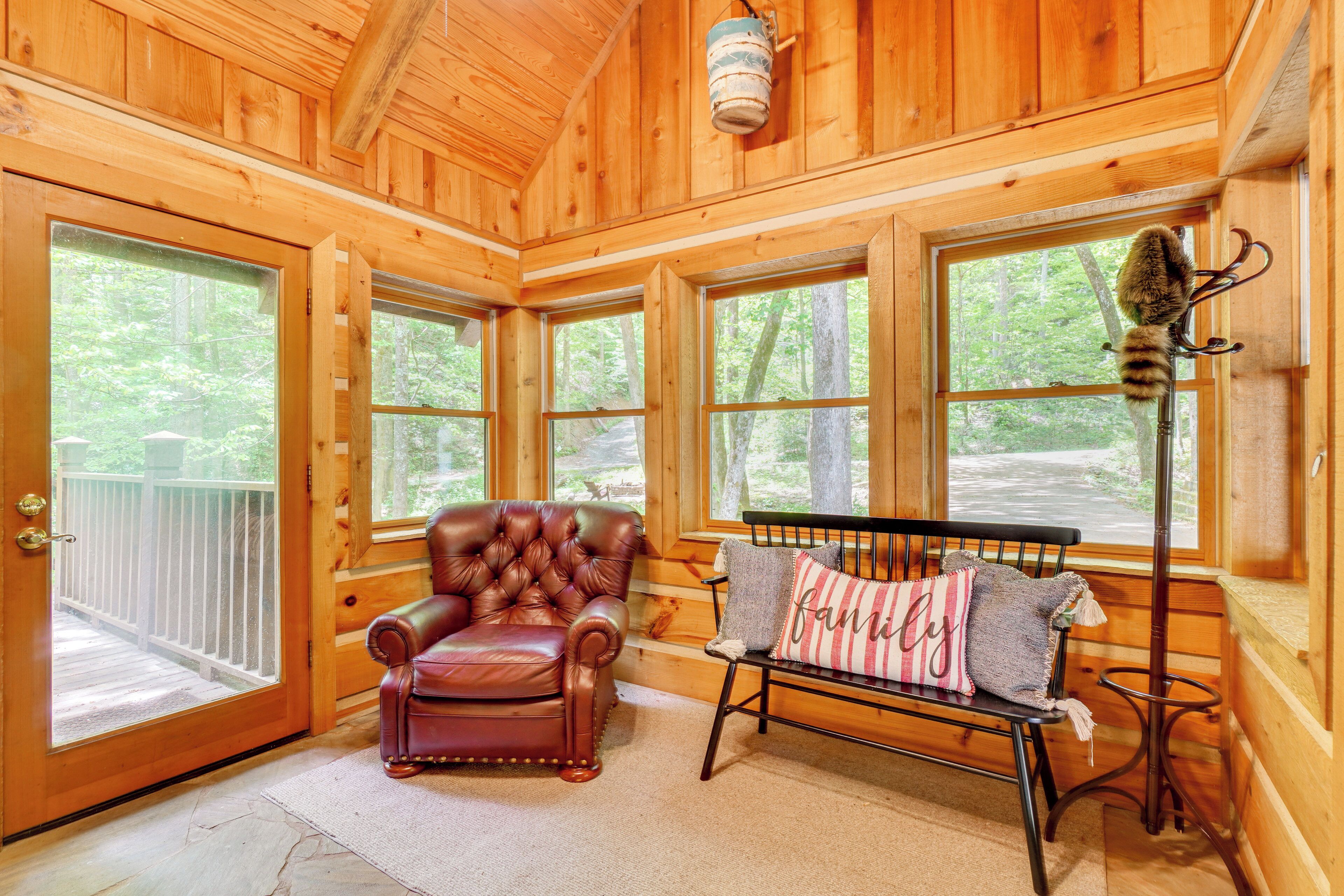 A wooden cabin interior with a leather armchair, a bench with pillows, and a window with a hanging lamp.