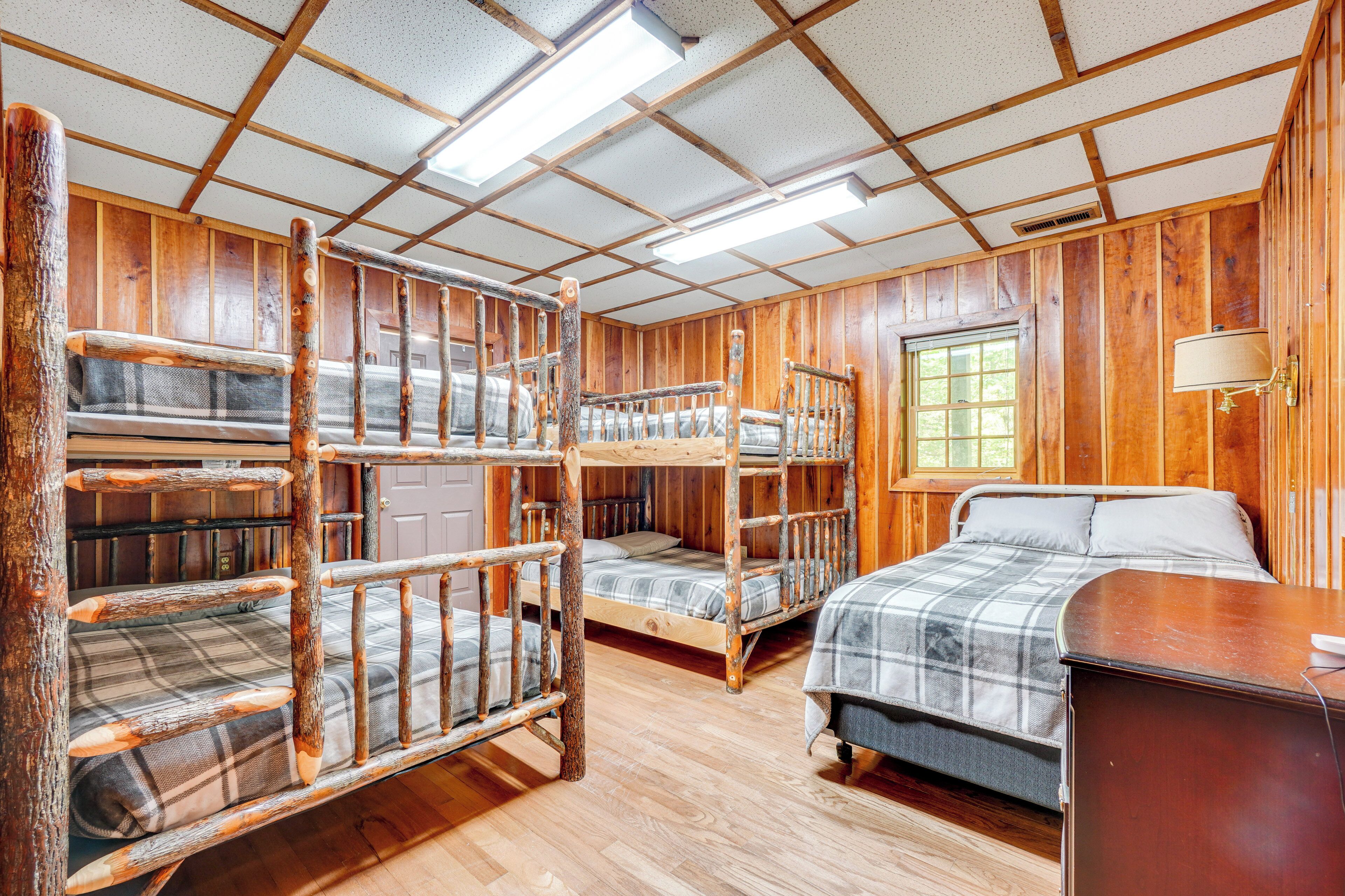 A cabin-style room with wooden walls, bunk beds, a single bed, and a window.
