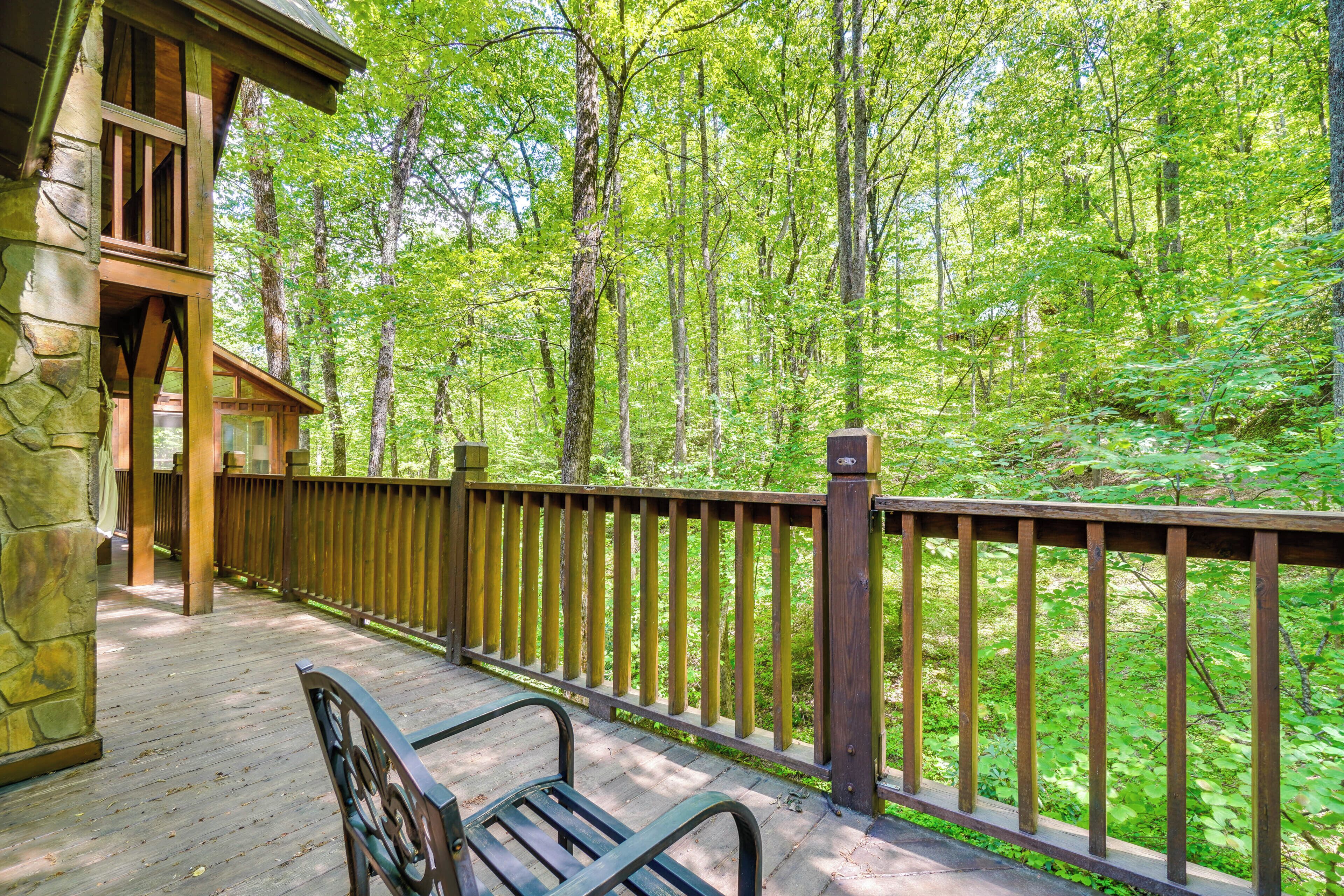 A wooden deck with a stone pillar, a bench, and a wooden fence overlooking a forest.