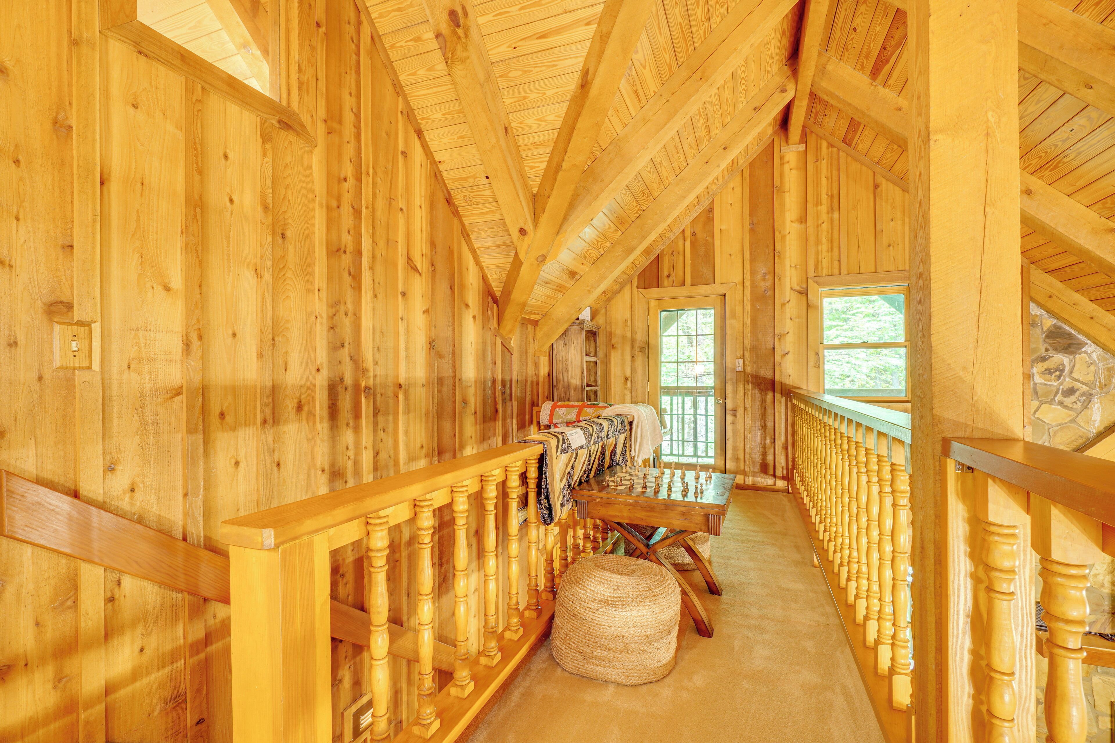 A wooden interior with a long dining table and chairs, a staircase with wooden balusters, and a stone wall.