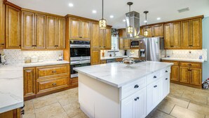 A spacious kitchen with wooden cabinets, a large island, stainless steel appliances, and pendant lighting. - Outdoor Kitchen & Hot Tub: Tranquil Home in Humble (Humble)