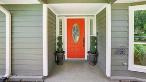 A house entrance with a red door, two potted topiary plants, and a decorative metal piece on the wall. - Outdoor Kitchen & Hot Tub: Tranquil Home in Humble (Humble)
