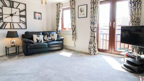 A living room with a black leather sofa, a flat-screen TV, and a patterned curtain. - 63 Severn Street (Bridgnorth)