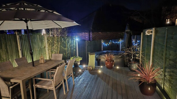 An outdoor patio with a wooden deck, a dining table with chairs, a large umbrella, and string lights. - 63 Severn Street (Bridgnorth)