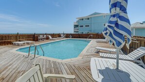 A pool area with a wooden deck, lounge chairs, and a pool. - Sandy Oceanfront 2nd FL 1BR W/pool at The Riggings (Kure Beach)