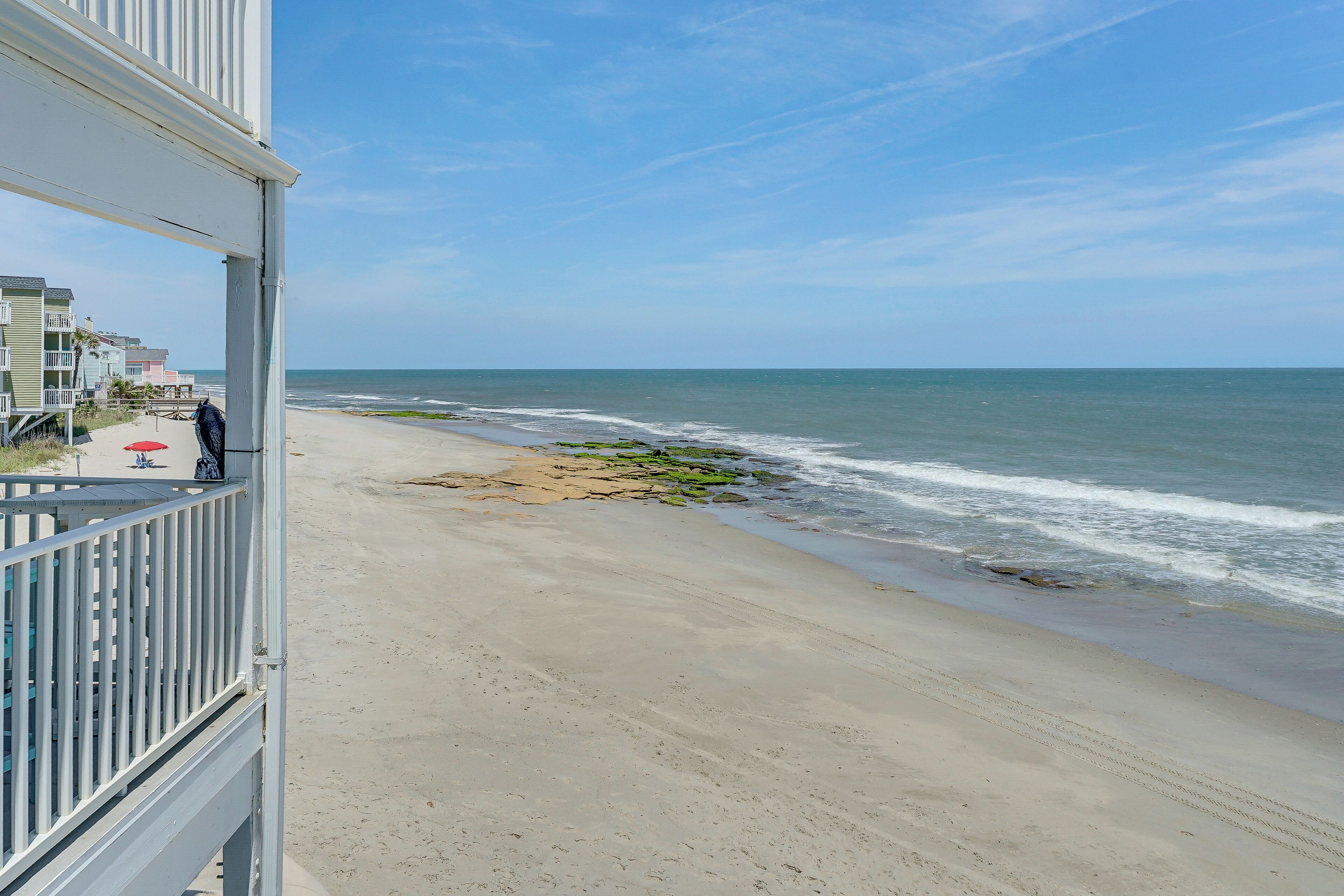 Une vue sur la plage depuis un balcon doté d’une balustrade, avec une plage de sable et des vagues déferlantes.