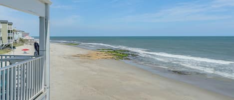 A beach view from a balcony with a railing, a sandy beach, and ocean waves.
