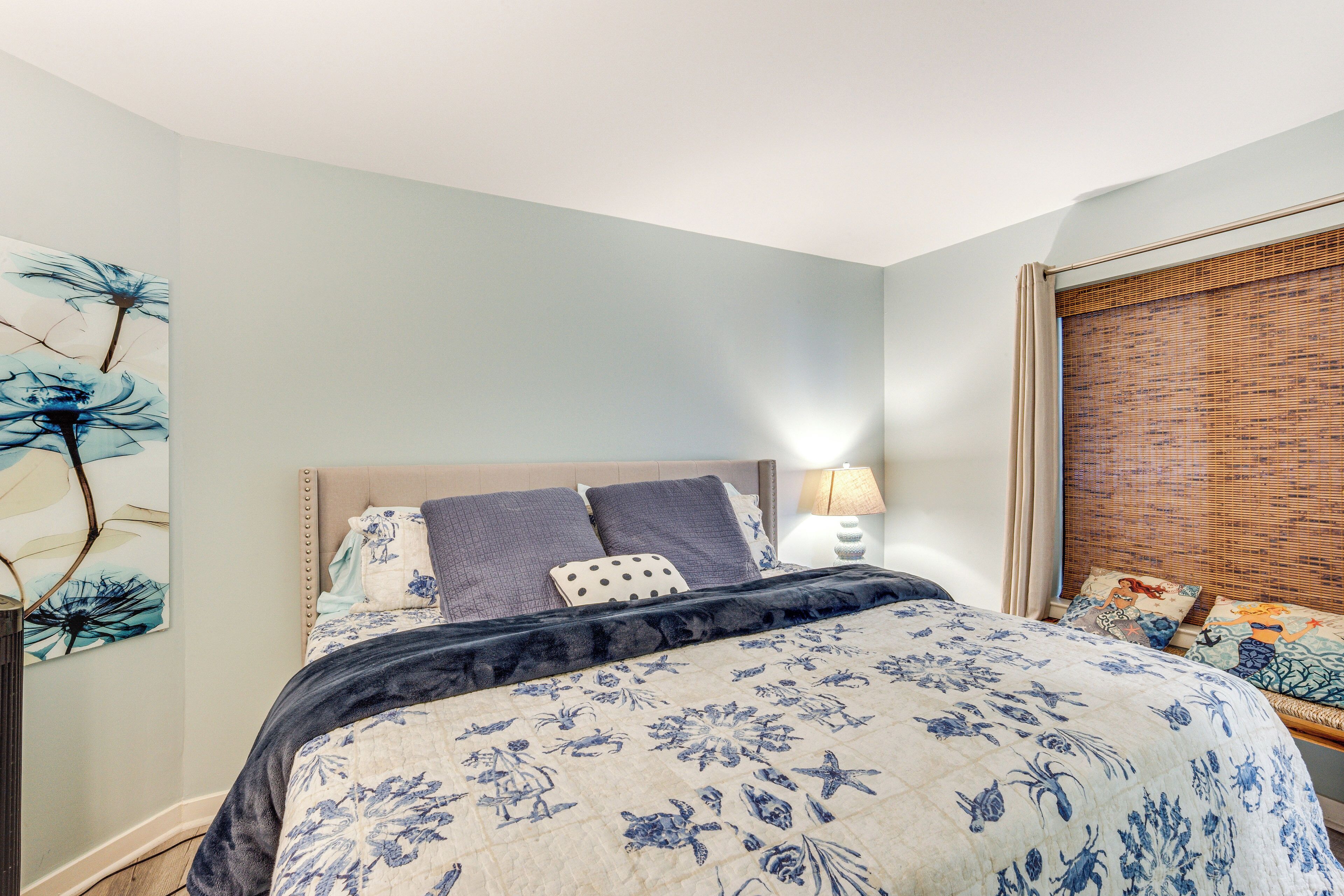 A bedroom with a bed, a nightstand, a lamp, and a wall art piece.