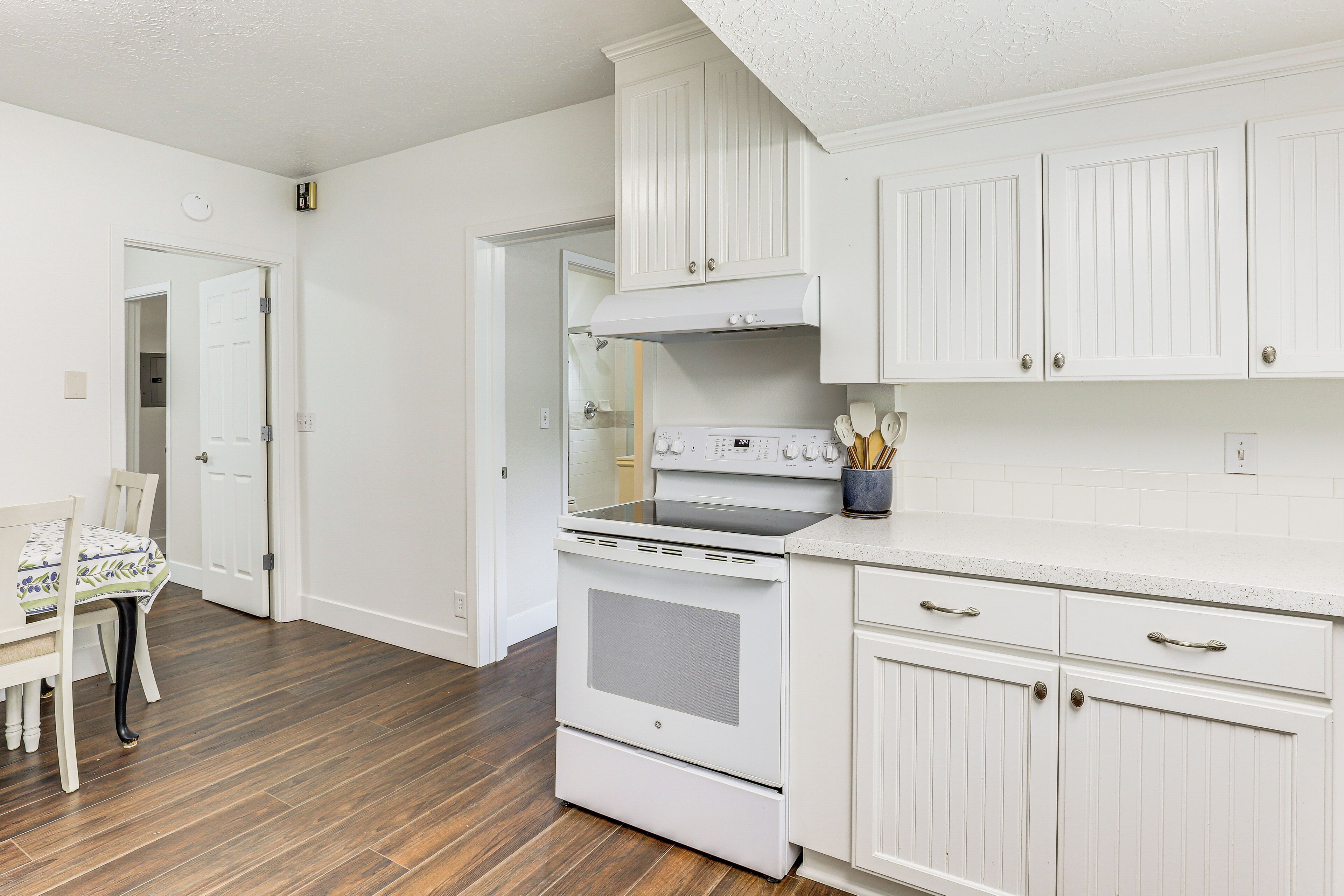 A kitchen with white cabinets, a stove, and a dining area with a table and chairs.