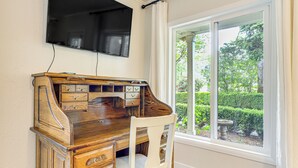 A wooden desk with drawers and a chair, a television mounted on the wall, and a window with a view of greenery. - 8 Mi to Columbia River Gorge: Cottage w/ Deck! (Gresham)