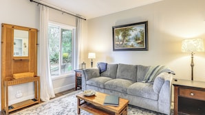 A living room with a sofa, a coffee table, a lamp, a painting, and a window with curtains. - 8 Mi to Columbia River Gorge: Cottage w/ Deck! (Gresham)