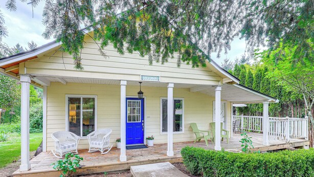 A house with a porch, two white wicker chairs, a blue door, and a small garden area. - 8 Mi to Columbia River Gorge: Cottage w/ Deck! (Gresham)