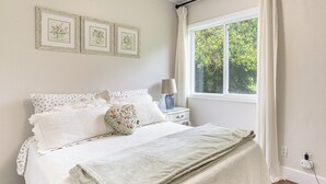 A neatly made bed with a white and green blanket, a floral pillow, and a bedside table with a lamp. - 8 Mi to Columbia River Gorge: Cottage w/ Deck! (Gresham)