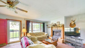Una sala de estar con sofá, sillón, mesa de centro, chimenea, televisor y ventilador de techo.