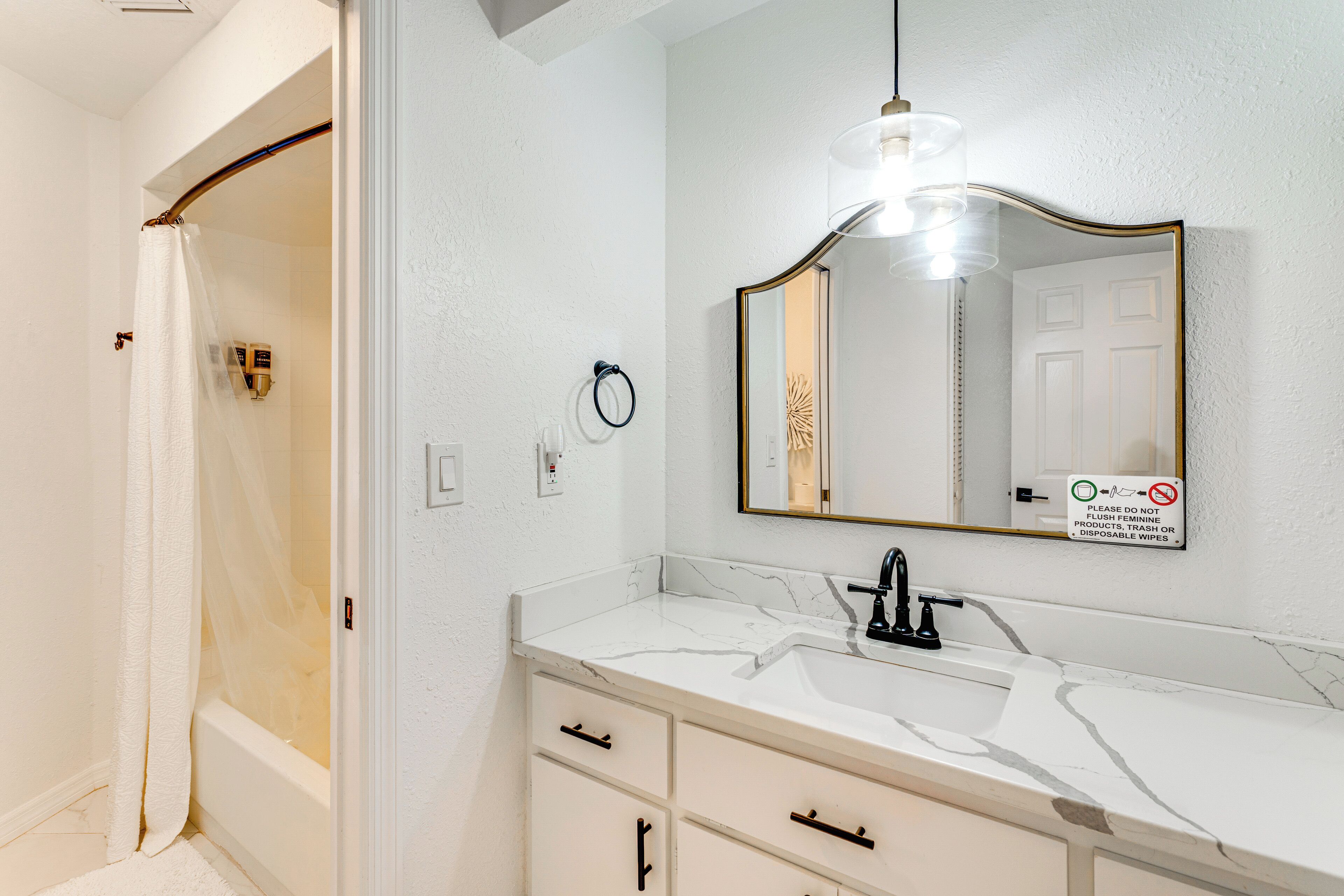 Un bagno con un lavabo in marmo bianco, uno specchio con cornice dorata e una tenda da doccia.