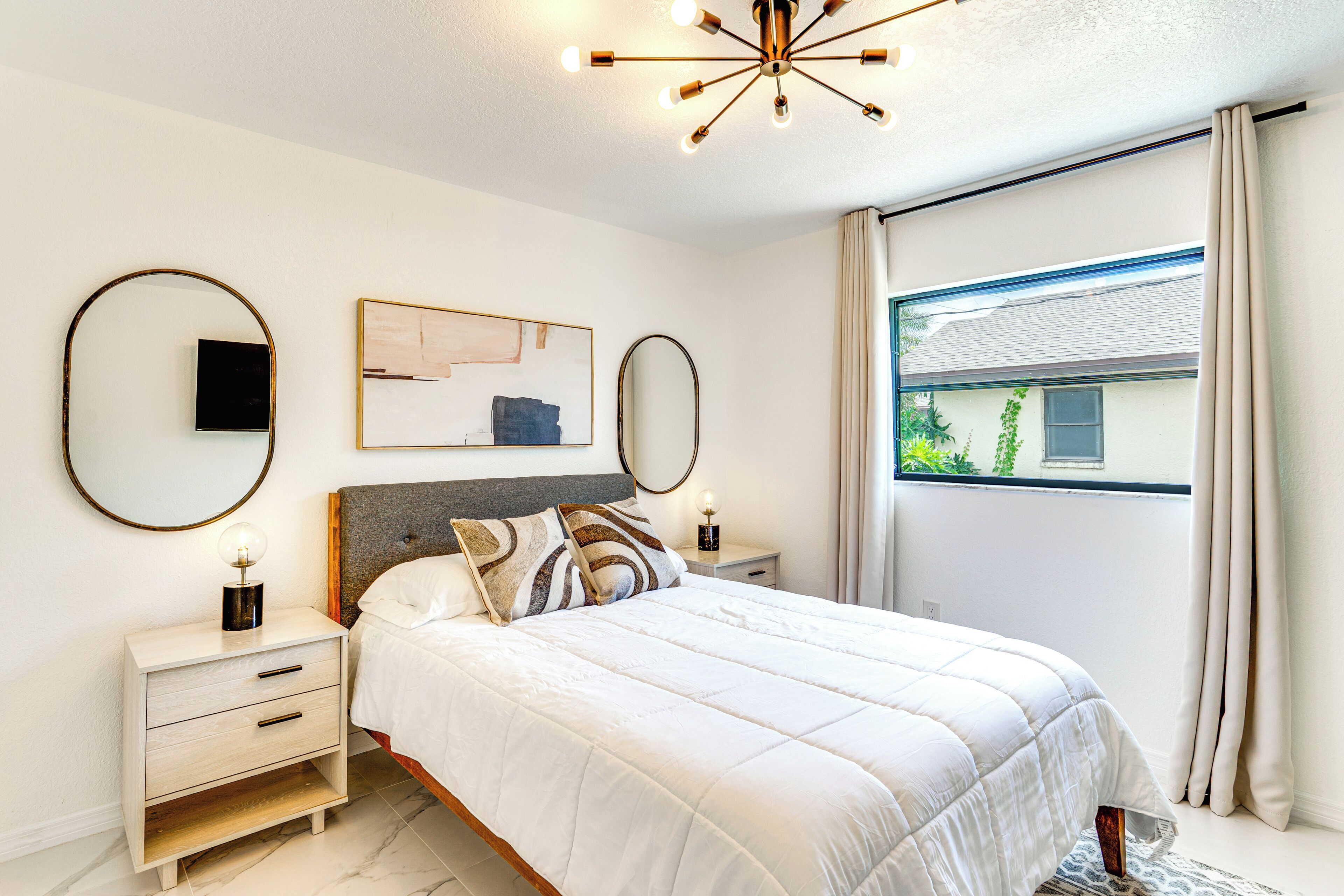 A bedroom with a bed, bedside tables, a mirror, and a ceiling light fixture.